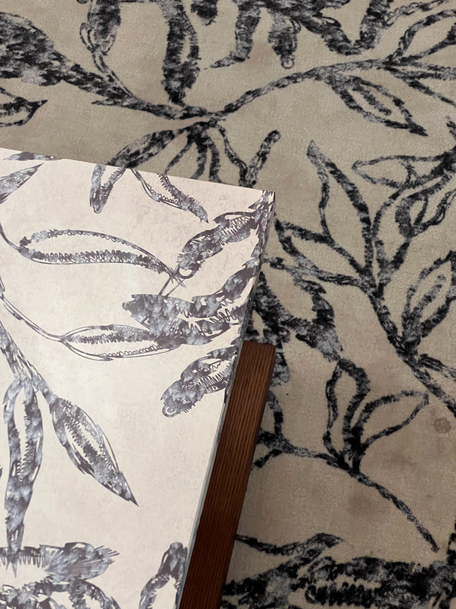Close-up of the illustrated coffee-table surface and its edge beside patterned textiles.