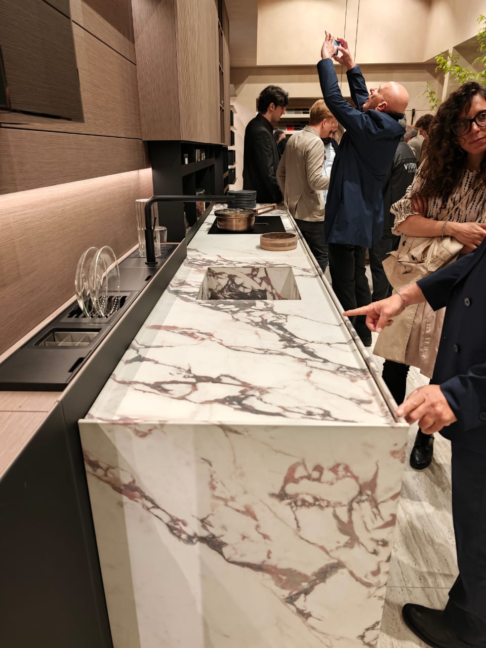 Visitors looking at a coordinated veined countertop and basin at a design exhibition.